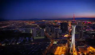 The Las Vegas Strip from the air at dusk, the STRAT tower lit white and the city lights running to the mountains