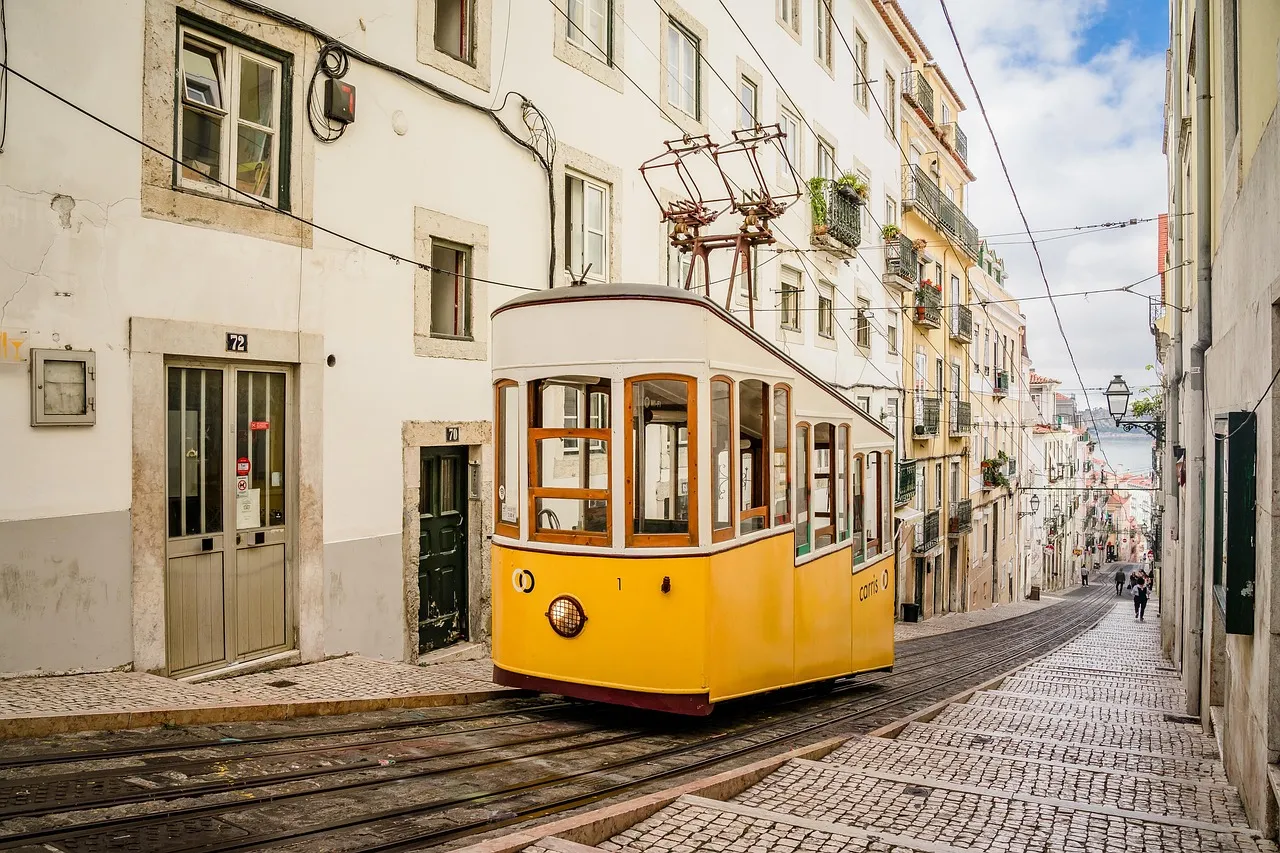 A yellow Lisbon tram climbing a narrow cobbled street between pale old houses in Alfama
