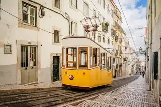 A yellow Lisbon tram climbing a narrow cobbled street between pale old houses in Alfama