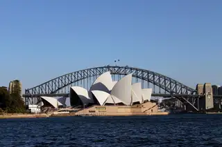 The Sydney Opera House seen from the harbour, with the Sydney Harbour Bridge behind it under a clear blue sky