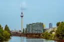 Der Berliner Fernsehturm über Bürogebäuden und einem grünen Spreeufer