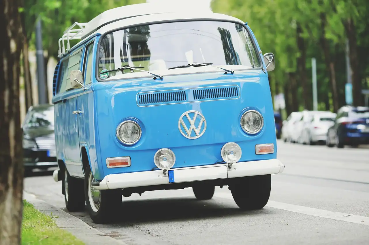 Ein blauer VW-Oldtimerbus am Straßenrand unter Bäumen