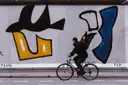 Ein Radfahrer an einem bemalten Stück der Berliner Mauer