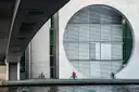 Drei Radfahrer an der Spree vor einem Regierungsbau aus Beton mit riesigem Rundfenster