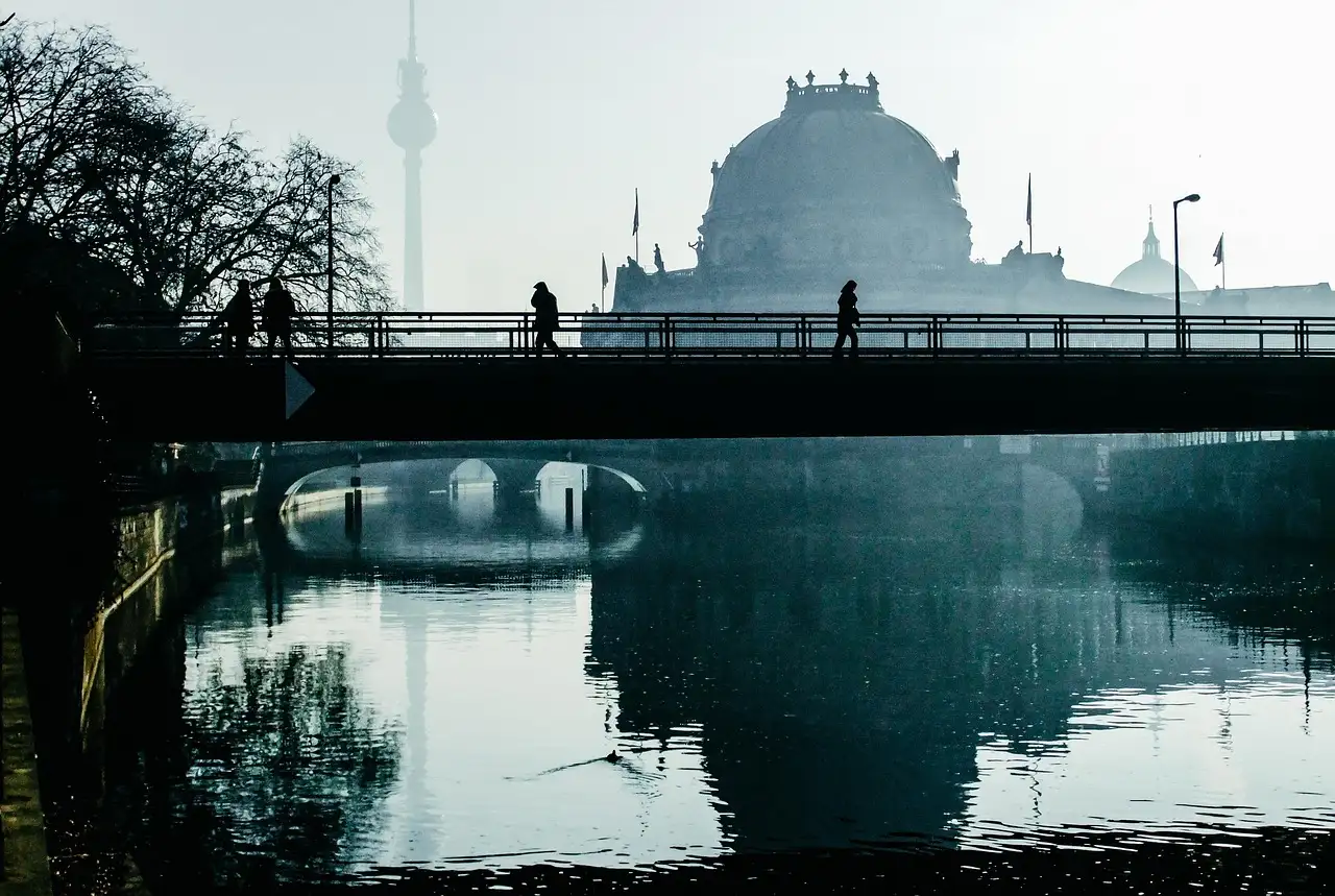 Menschen gehen an einem dunstigen Morgen über eine Spreebrücke, dahinter die Kuppel des Bode-Museums und der Fernsehturm