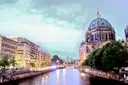 Die Spree in der Abenddämmerung mit beleuchteten Häusern am Ufer, rechts die Kuppel des Berliner Doms