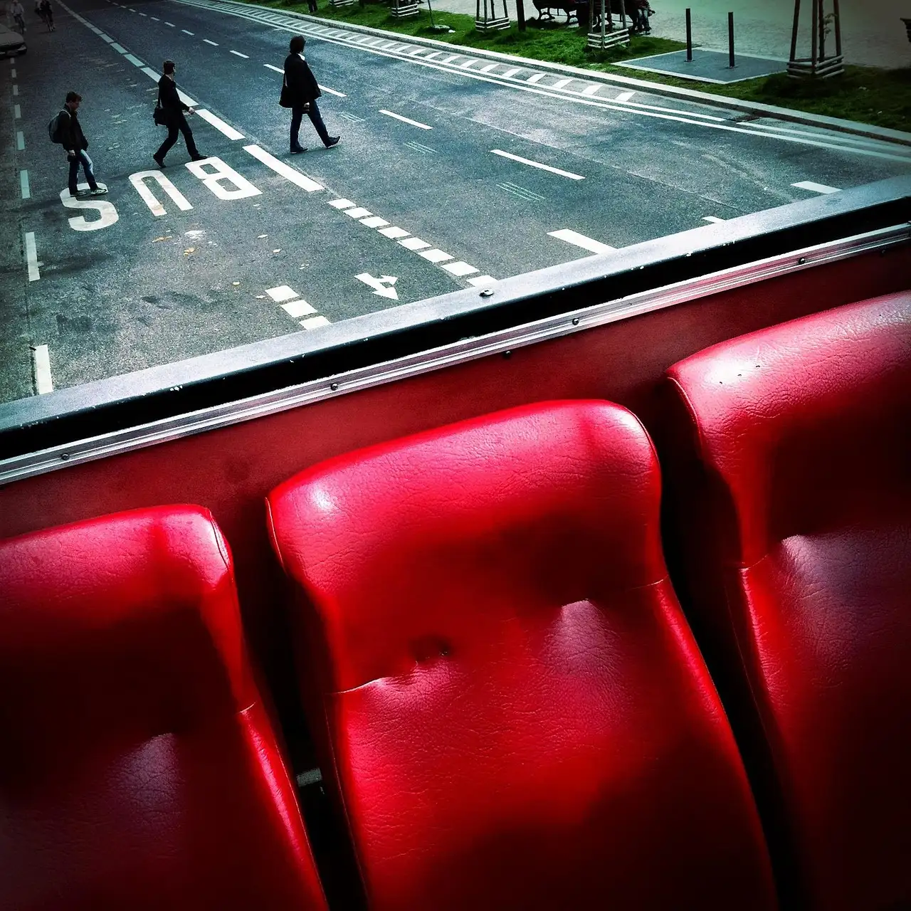 Drei rote Sitze auf dem Oberdeck eines offenen Sightseeing-Busses, darunter überqueren Leute die Straße