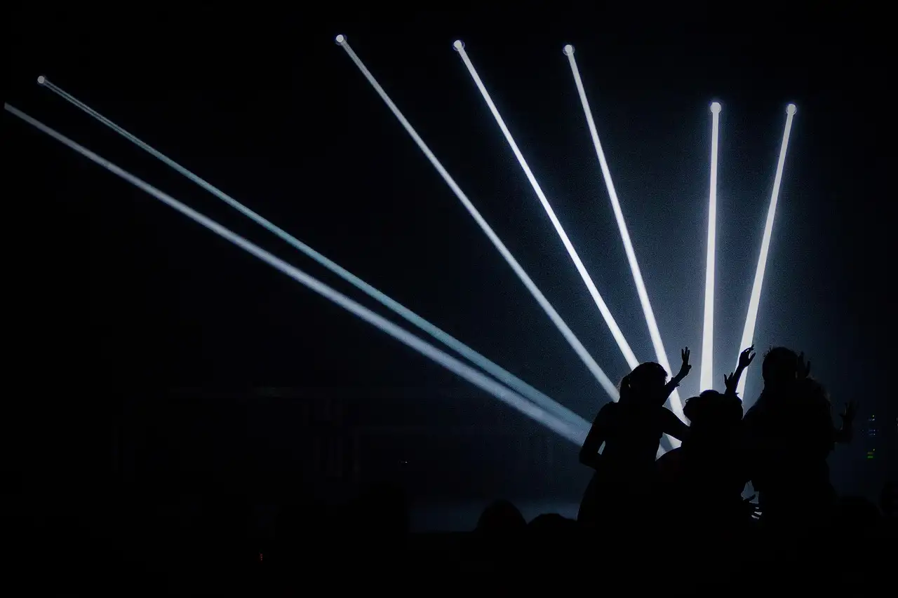 Weiße Lichtstrahlen in einem dunklen Club über den Silhouetten von Tanzenden