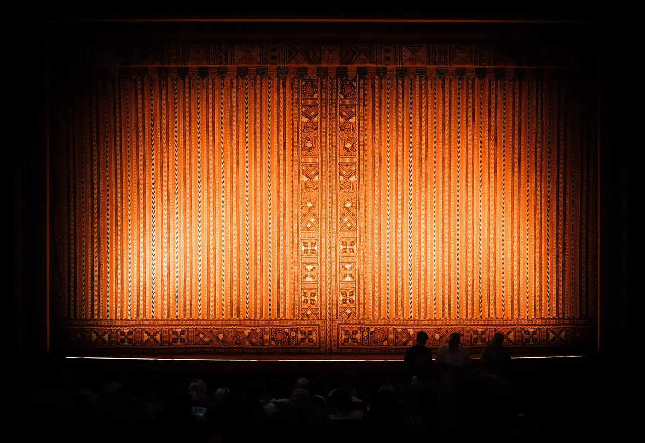 Eine leere Theaterbühne hinter einem leuchtend orangen Vorhang