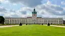 Schloss Charlottenburg mit grünem Kuppelturm hinter einer weiten Wiese unter bewölktem Himmel