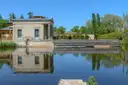 Ein helles klassizistisches Gartengebäude spiegelt sich in einem Teich im Park Sanssouci