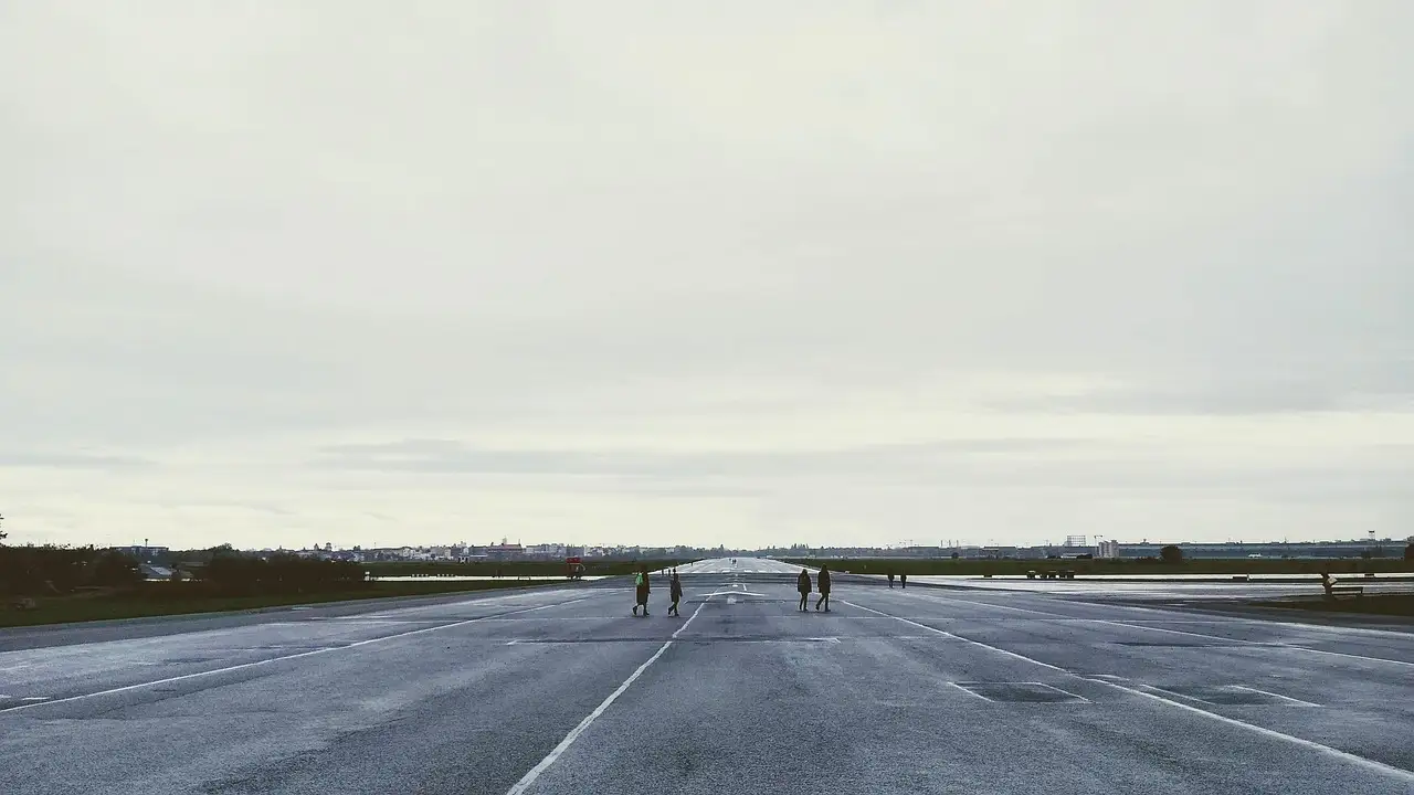 Die weite ehemalige Start- und Landebahn auf dem Tempelhofer Feld unter grauem Himmel, mit ein paar Menschen in der Ferne