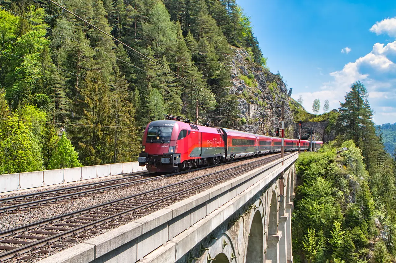 Ein roter österreichischer Railjet fährt über einen Steinviadukt zwischen bewaldeten Berghängen