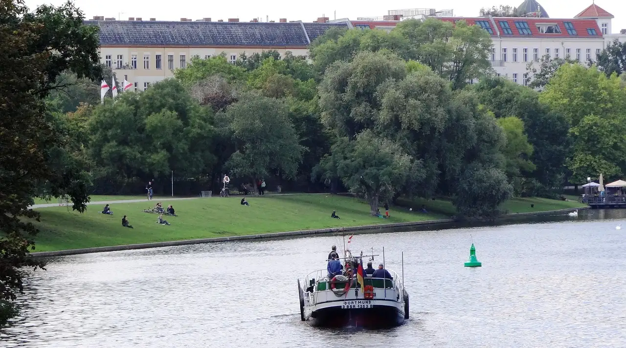 Ein kleines Boot auf dem Landwehrkanal, am Ufer sitzen Leute im Gras