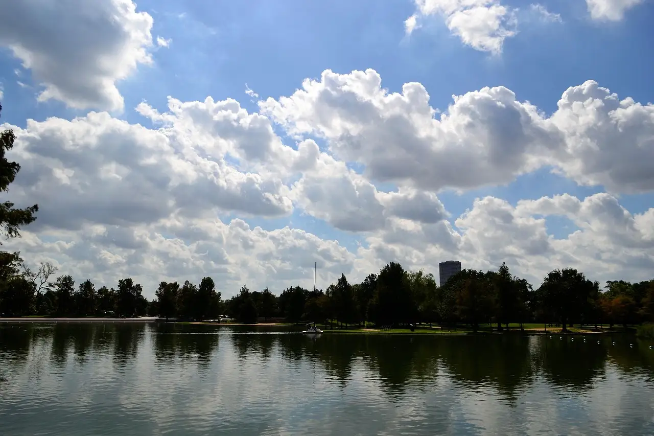 Ein See im Hermann Park in Houston, mit Bäumen am Ufer und einem weiten, wolkigen blauen Himmel