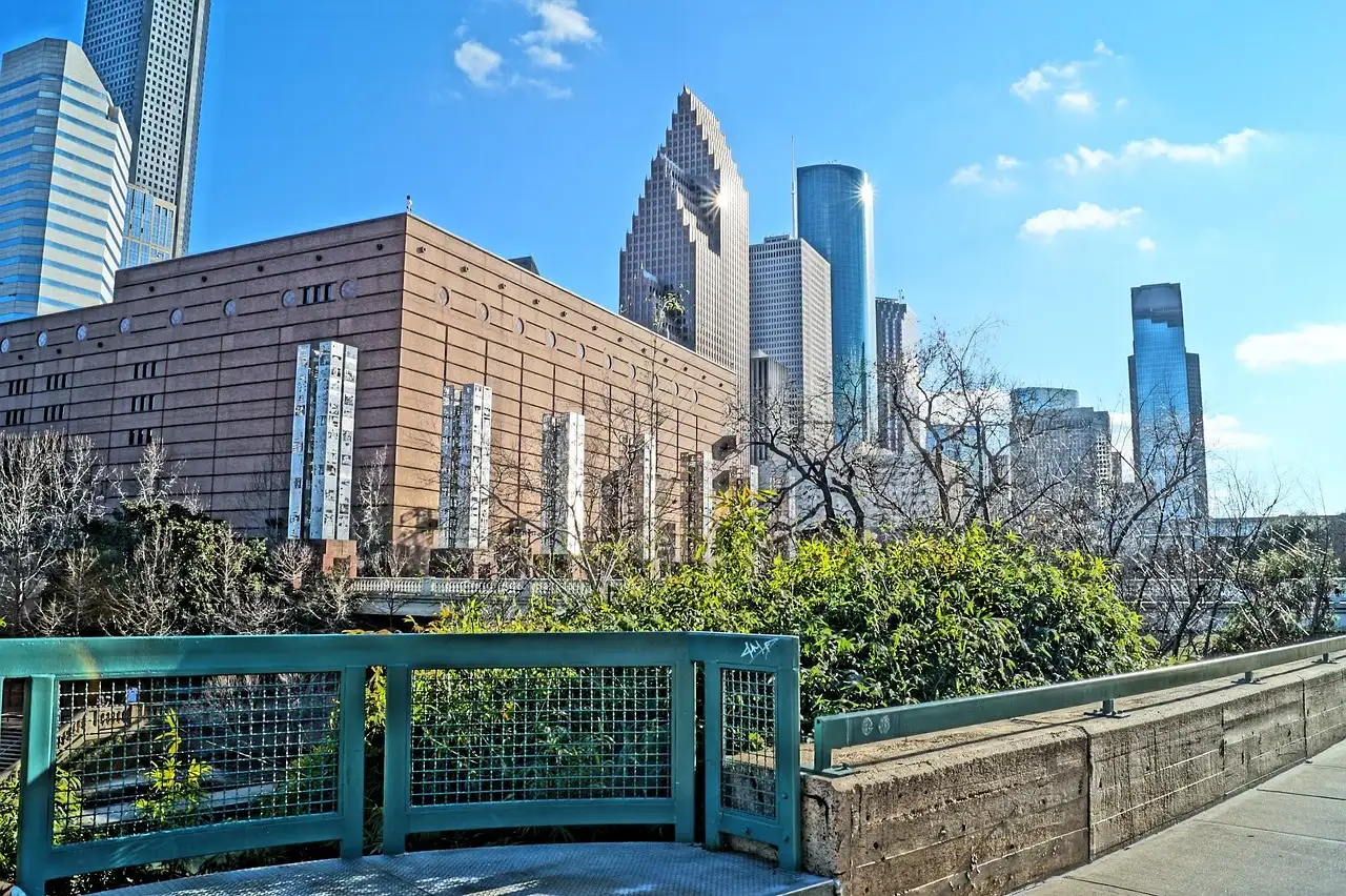 Die Türme von Downtown Houston ragen hinter Bäumen und einem Geländer in einem Stadtpark auf