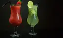 Ein roter Cocktail mit Erdbeere und ein grüner Cocktail mit Limette in hohen Gläsern vor Schwarz