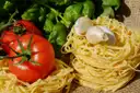 Nester frischer Eiernudeln neben reifen Tomaten, Knoblauch und Basilikum