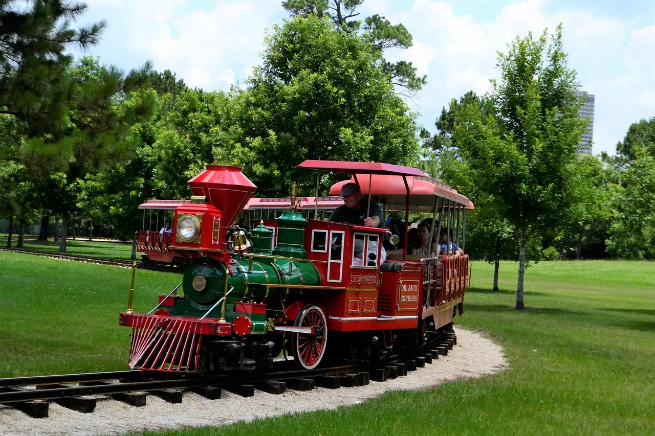 Ein rot-grüner Miniaturzug fährt mit Kindern durch einen grünen Park in Houston