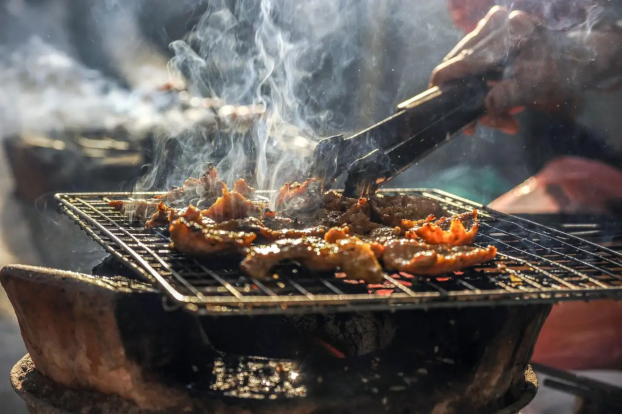 Fleisch gart auf einem rauchigen offenen Grill und wird mit der Zange gewendet