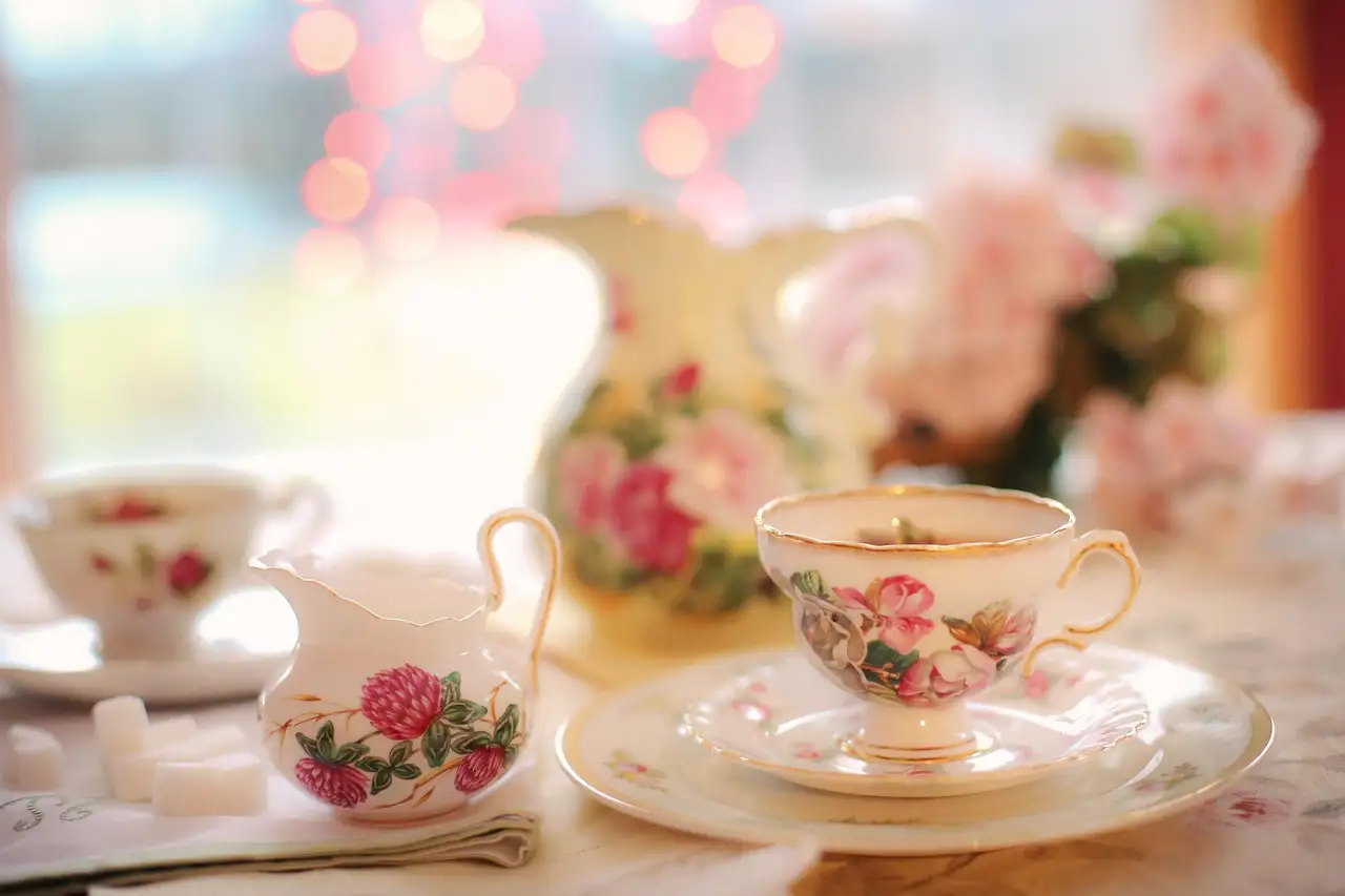 Ein Teeservice aus Porzellan mit rosa Blumen: Tassen, Milchkännchen und Würfelzucker