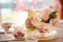 Ein Teeservice aus Porzellan mit rosa Blumen: Tassen, Milchkännchen und Würfelzucker