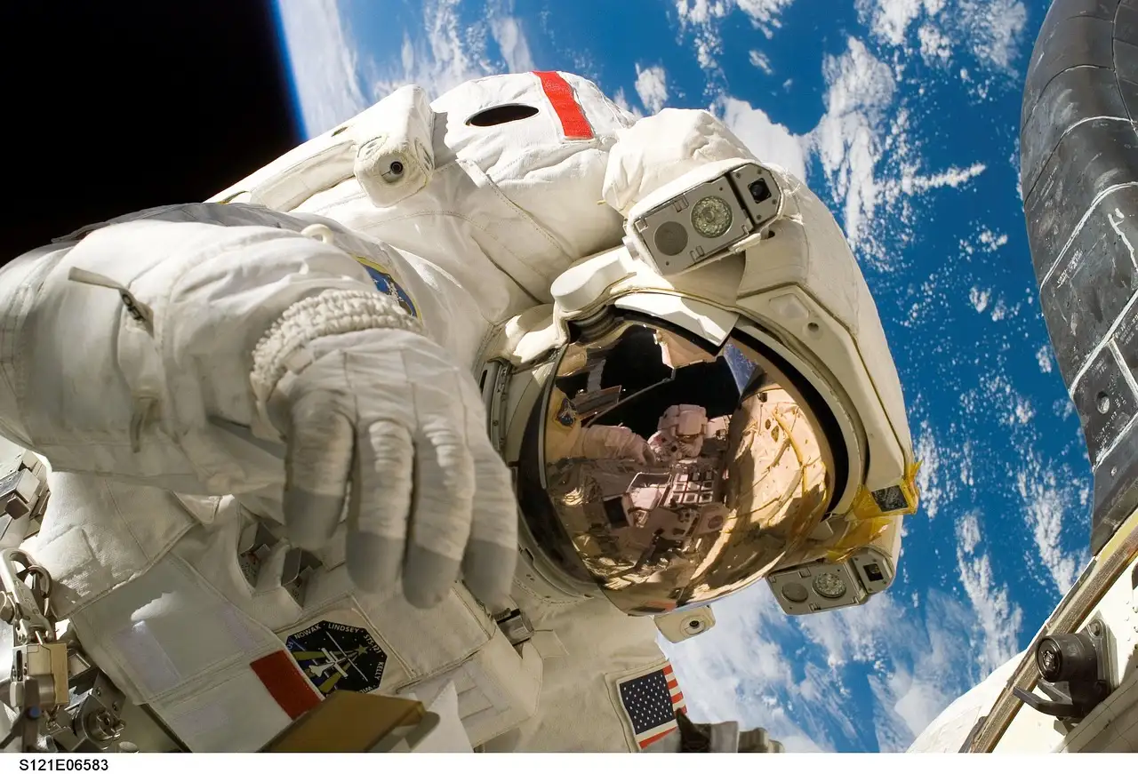 Ein Astronaut im weißen Raumanzug bei einem Außeneinsatz, dahinter die Erde und Wolken (NASA-Foto, allgemeines Weltraumbild)