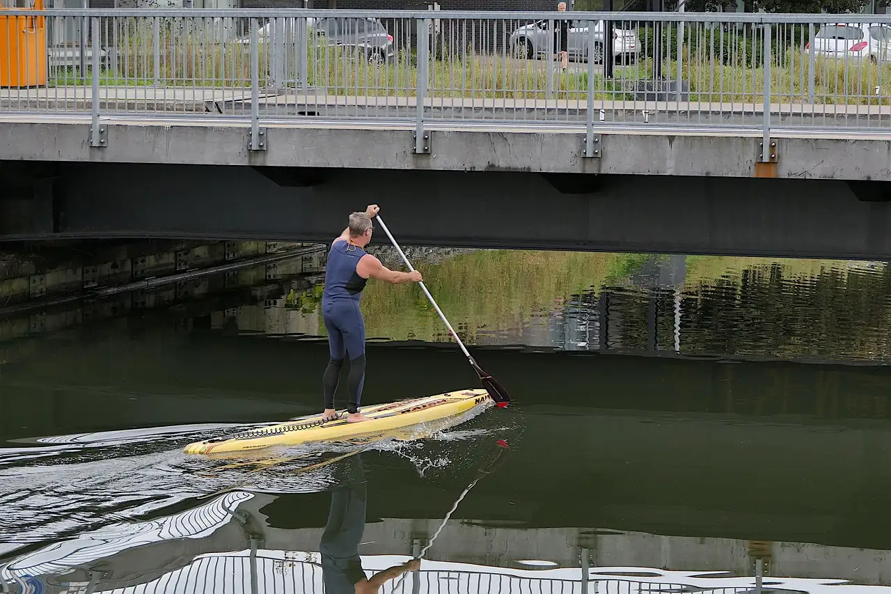 Ein Mensch auf einem Stand-up-Paddleboard fährt unter einer Brücke in der Stadt hindurch