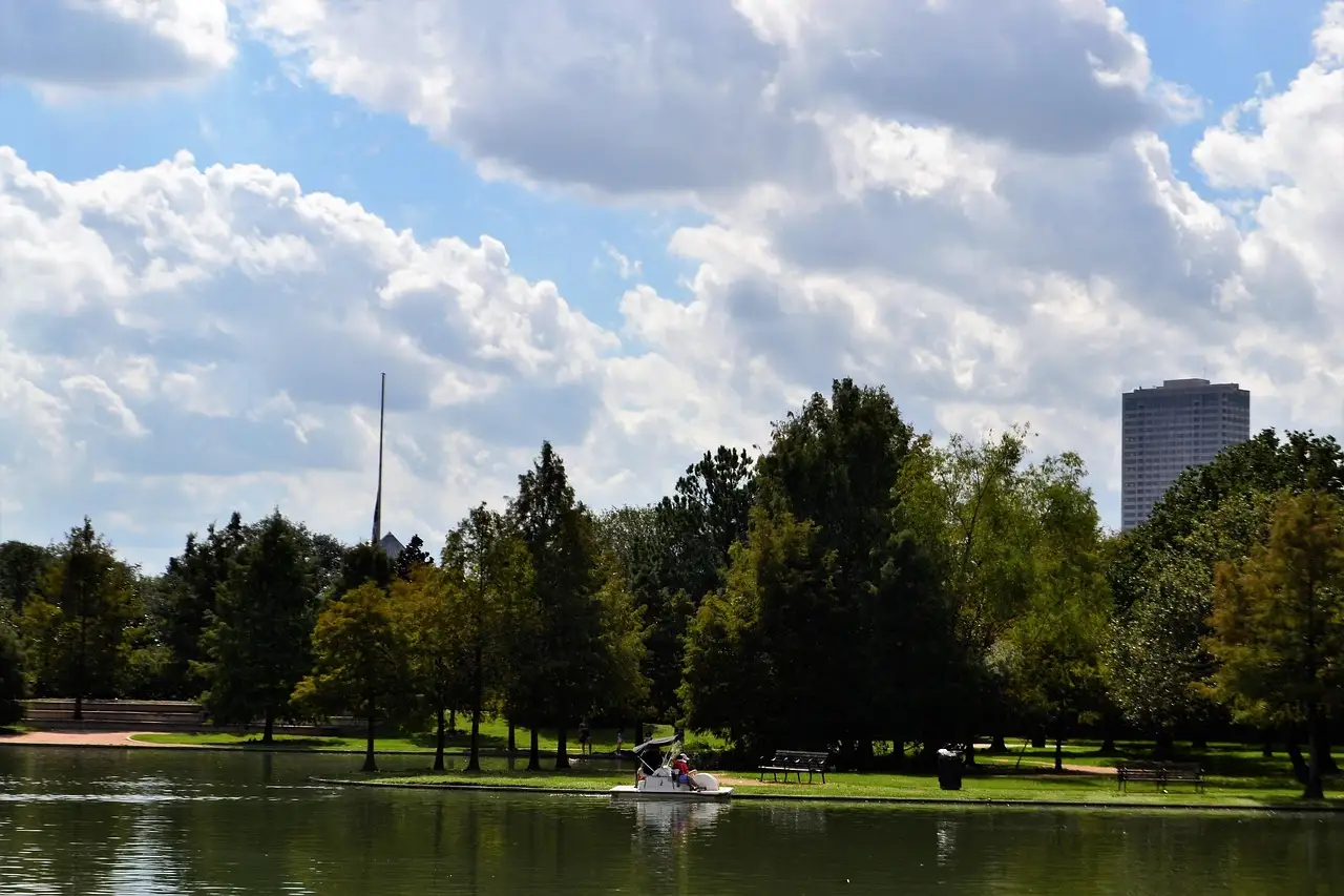 Ein kleines Boot auf dem See im Hermann Park in Houston, dahinter Bäume und ein Hochhaus