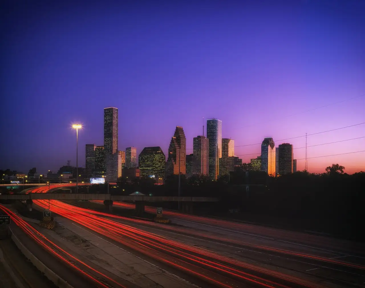 Die Skyline von Houston in der Dämmerung hinter einer Autobahn mit Lichtspuren, unter einem lila-rosa Himmel