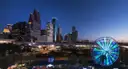 Die beleuchtete Skyline von Downtown Houston in der Dämmerung, davor ein leuchtendes Riesenrad