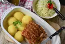 Schweinebraten mit Kartoffelknödeln und Krautsalat in einer weißen Schale