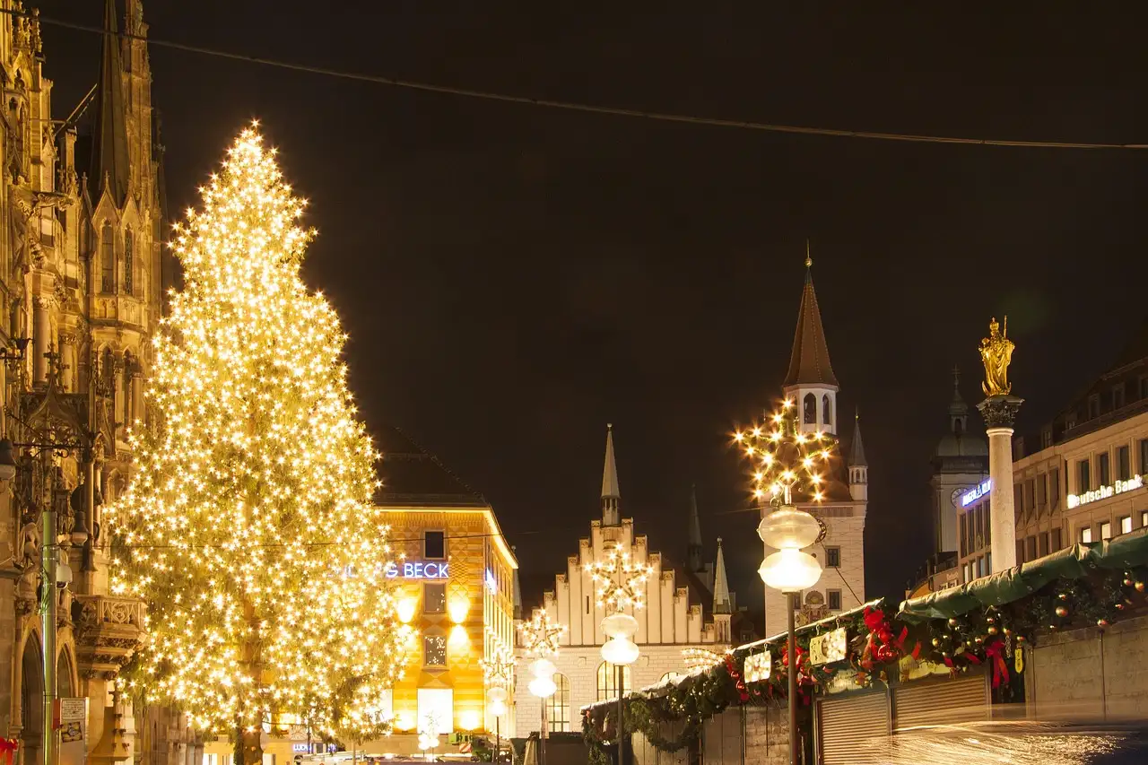 Ein hoher, beleuchteter Christbaum auf dem Marienplatz bei Nacht, neben dem Neuen Rathaus und Marktbuden