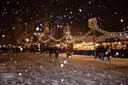 Schnee fällt nachts auf einen beleuchteten Weihnachtsmarkt