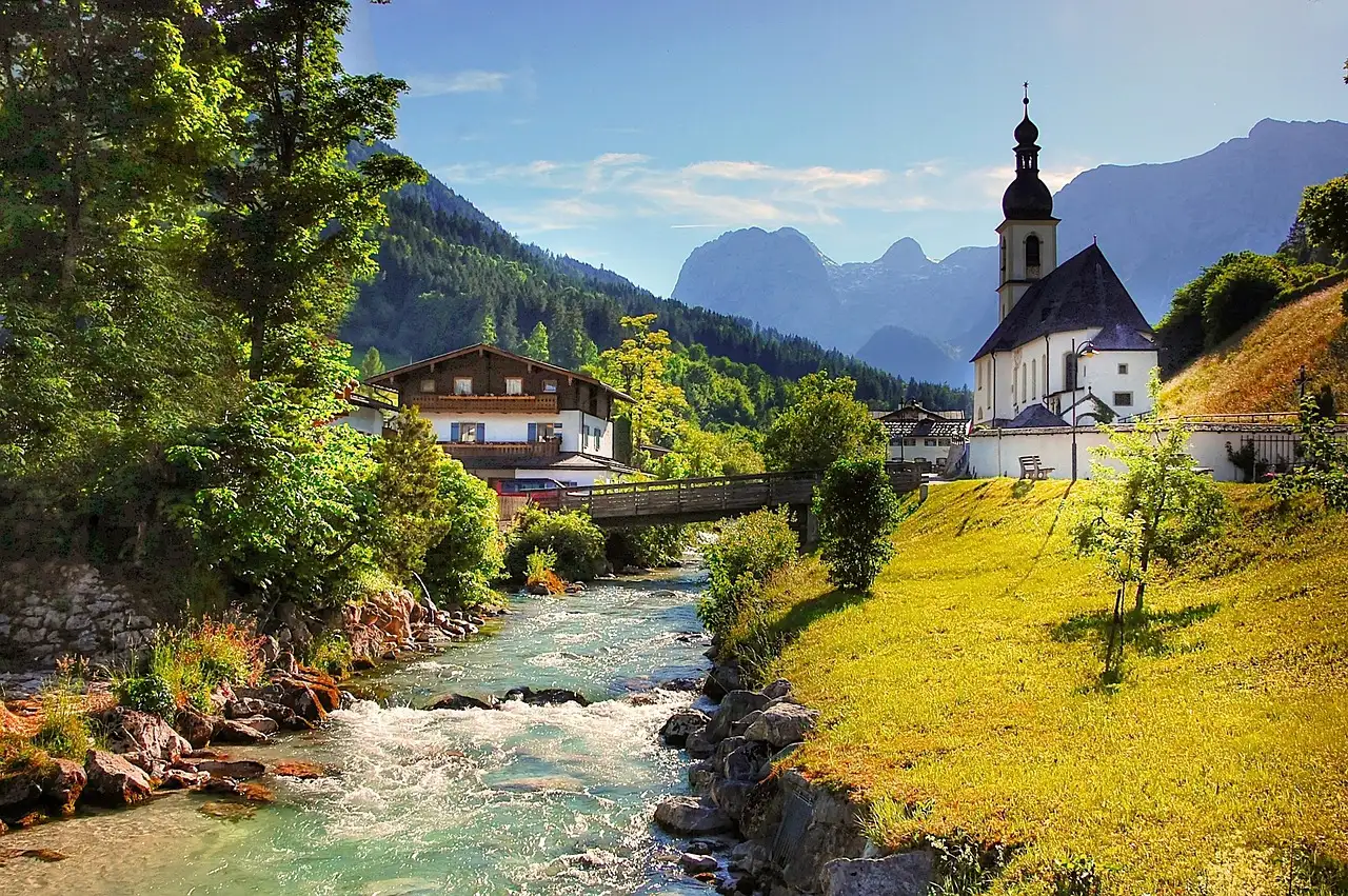 Die Kirche von Ramsau an einem Bergbach, dahinter felsige Gipfel