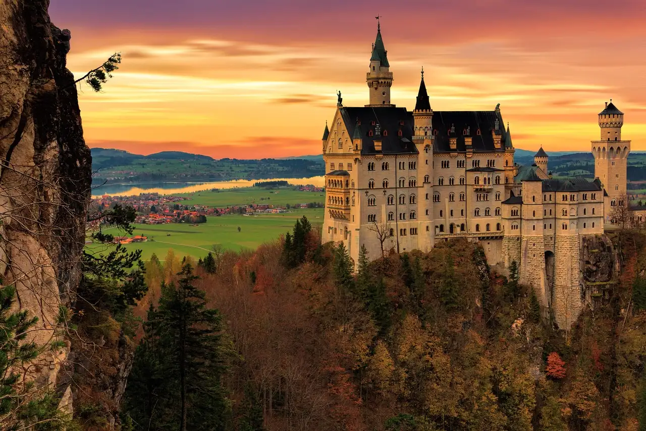 Schloss Neuschwanstein auf seinem Hügel im Abendlicht, darunter Herbstbäume