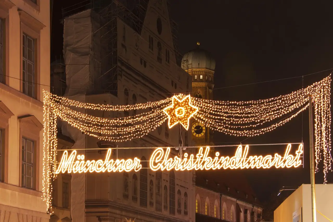 Der leuchtende Schriftzug „Münchner Christkindlmarkt“ über einer Straße bei Nacht