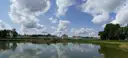 Schloss Nymphenburg jenseits eines breiten Sees unter blauem Himmel, die lange Front und die roten Dächer spiegeln sich im Wasser