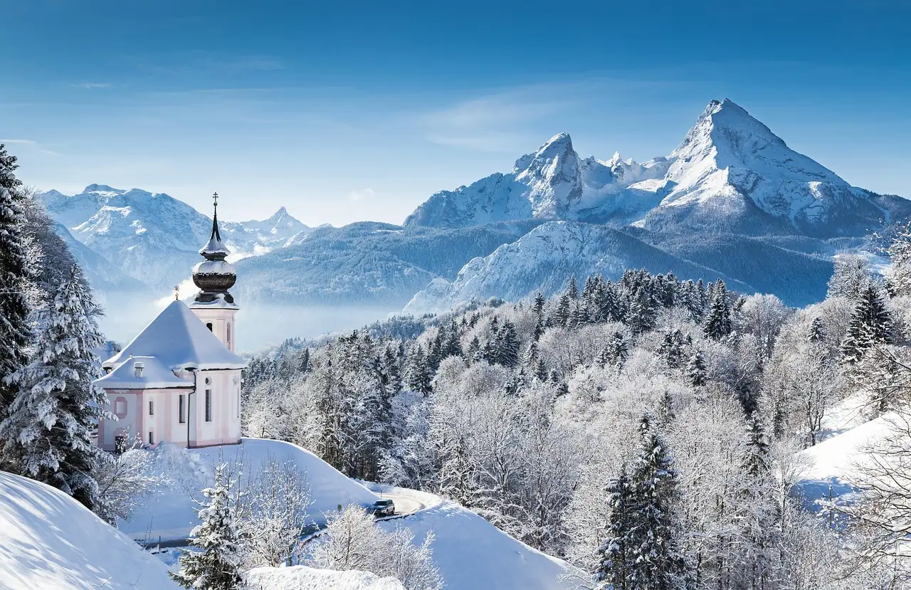 Eine kleine Kirche auf einem verschneiten Hügel vor den bayerischen Alpen