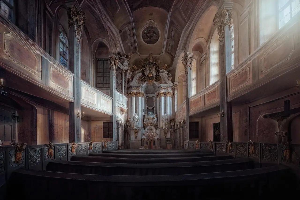 Eine dämmrige Barockkapelle mit goldenem Altar, Emporen und Kirchenbänken