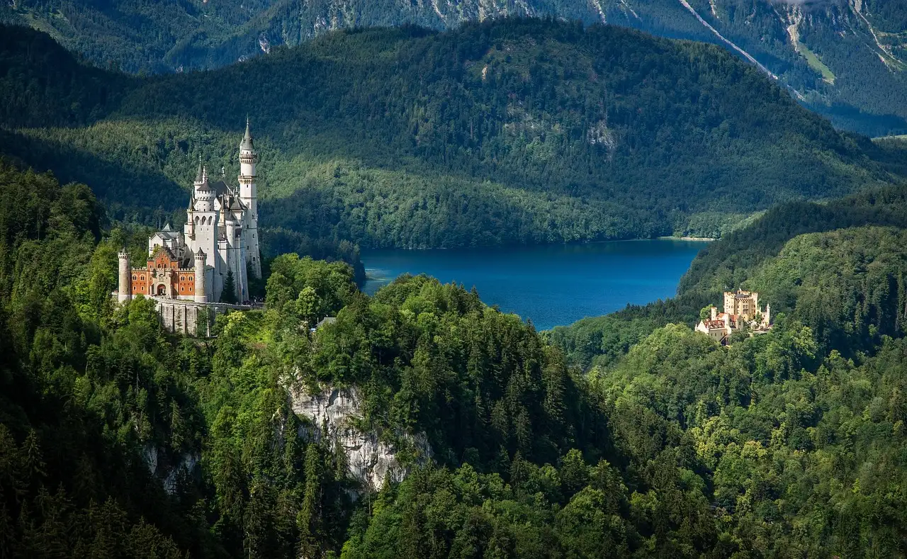 Schloss Neuschwanstein über dem Wald, darunter der Alpsee und Schloss Hohenschwangau