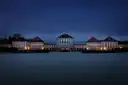 Schloss Nymphenburg zur blauen Stunde beleuchtet, gespiegelt im dunklen Wasser davor