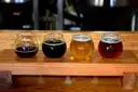 Vier kleine Gläser helles und dunkles Bier auf einem Probierbrett aus Holz