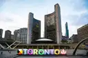 Die geschwungenen Türme des Rathauses von Toronto hinter dem bunten TORONTO-Schriftzug auf dem Nathan Phillips Square