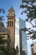 Der Uhrturm der Old City Hall in Toronto neben einem gläsernen Büroturm, umrahmt von Laub