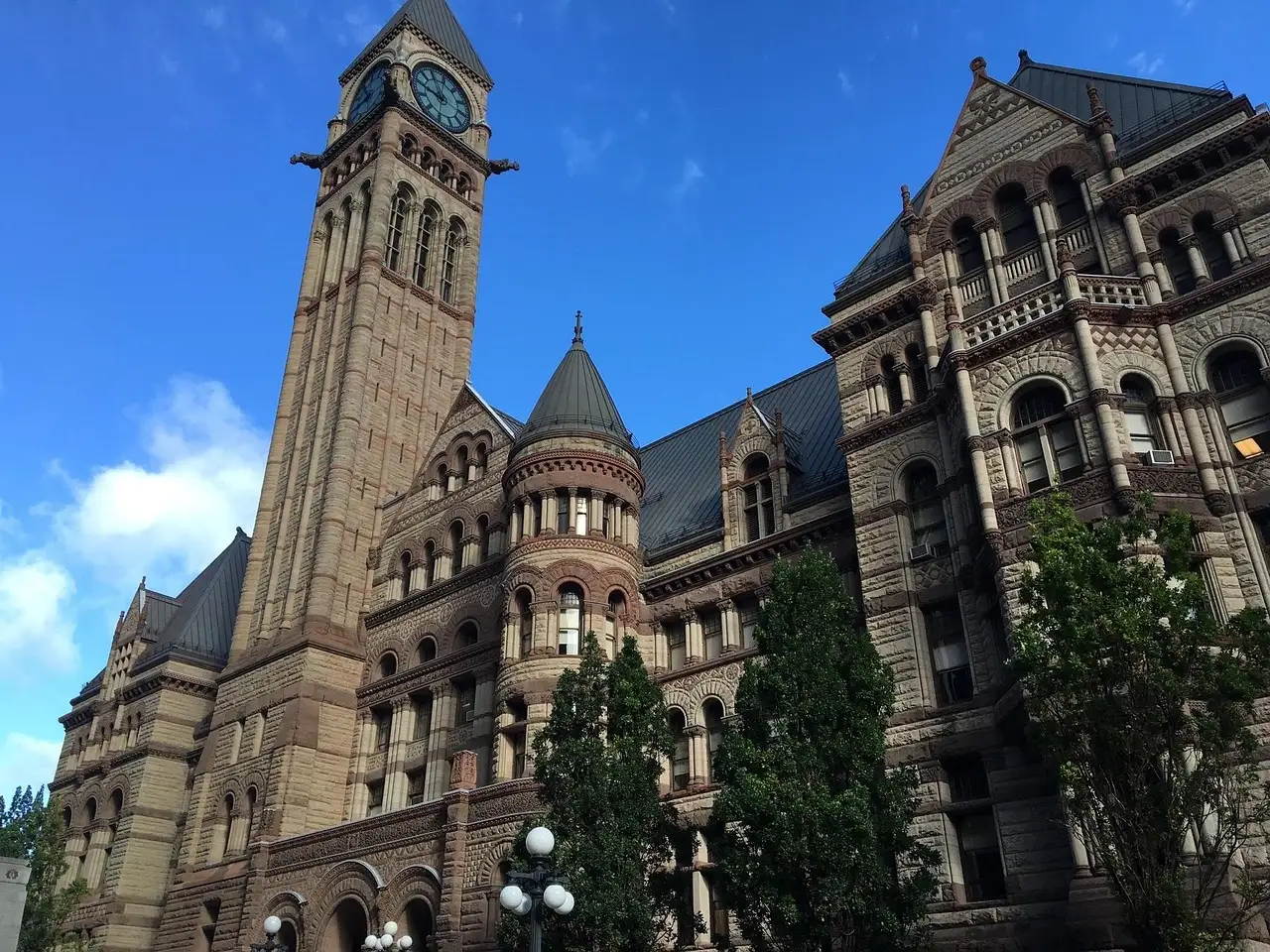 Uhrturm und Steinfassade der Old City Hall in Toronto unter blauem Himmel