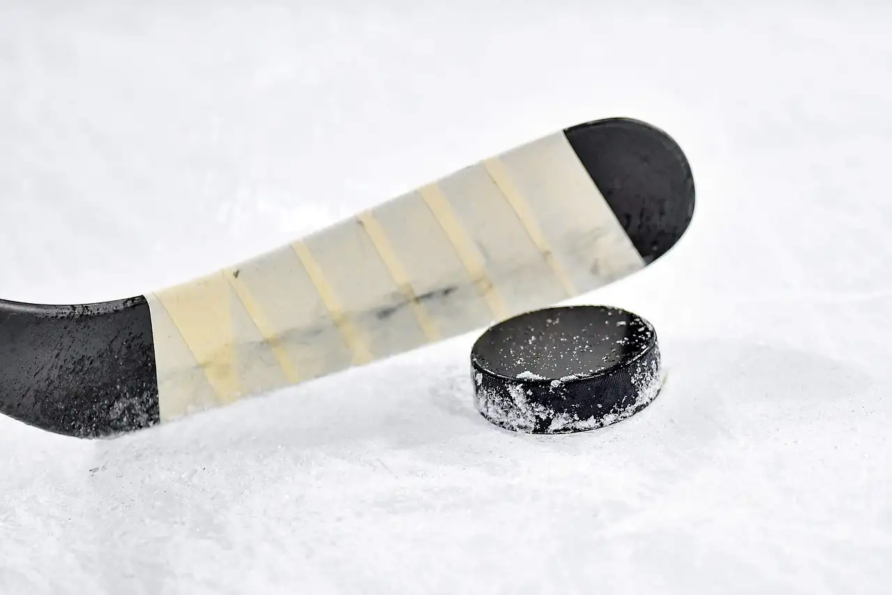 Ein Hockeyschläger mit Tape neben einem schwarzen Puck auf weißem Eis
