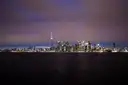 Torontos beleuchtete Skyline und der CN Tower über dunklem Wasser bei Nacht, unter lila Himmel.