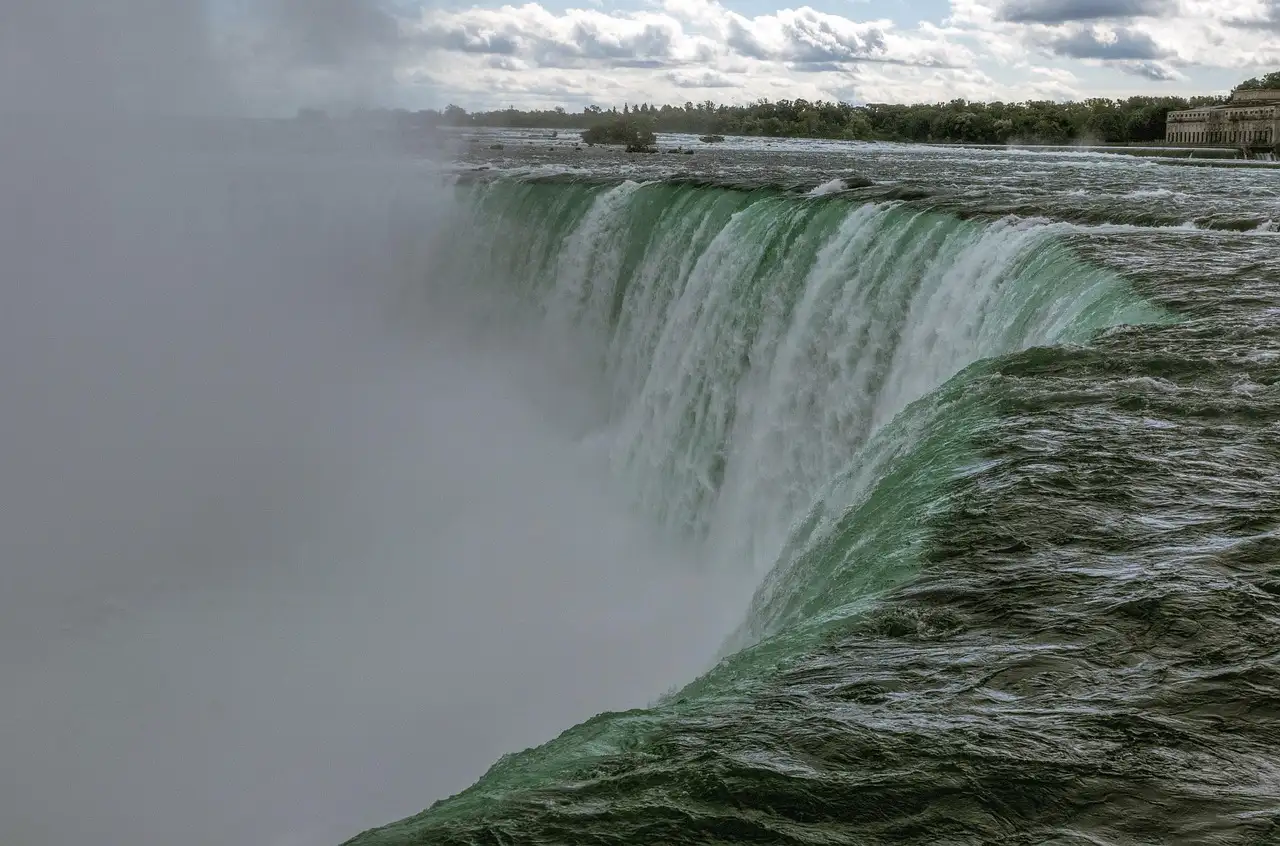 Wasser stürzt über die Kante der Horseshoe Falls in eine Gischtwolke, vom Ufer daneben gesehen
