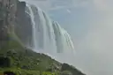 Eine Wand aus fallendem Wasser und Gischt von unten, neben einem grünen Hang